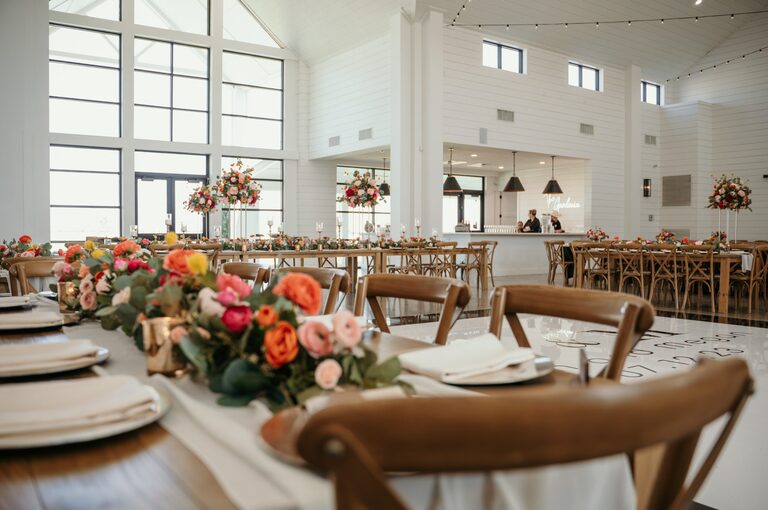 Wooden wedding reception tables with elegant place settings, colorful floral garlands and tall centerpieces.
